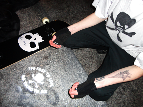zoom sur les bras d'un jeune homme sur fond de bitume, de graffiti blanc et de skateboard