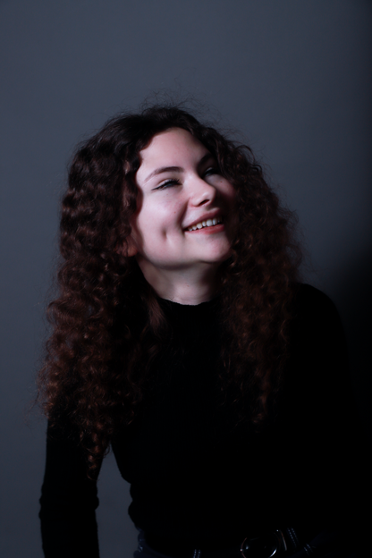 photo de jeune fille souriante et de profil aux cheveux bouclés et aux yeux bleus