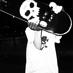 photo en noir et blanc d'un jeune homme avec un skate et un tshirt tête de mort