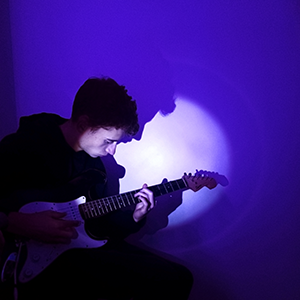 photo de jeune homme qui joue de la guitare dans une ambiance violette